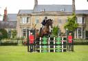 Helen West jumping in the arena in front of Southfield House at Nunney International Horse Trials