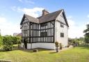 Timber-framed house with black and white cladding overlooking lawn and patio seating