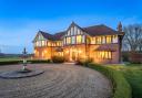 Front elevation at dusk with lit windows, gravel drive and fountain