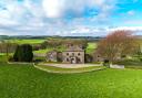 An aerial view of the property set within its own grounds, surrounded by open green fields and rolling countryside