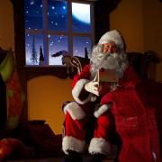 Santa holding a bag full ofchristmas gifts. He is sitting in his animated grotto. Horizontal image.