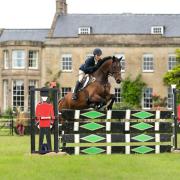 Helen West jumping in the arena in front of Southfield House at Nunney International Horse Trials