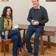 Silversmith Karina Gill and furniture designer-maker Simon Thomas Pirie. Karina is seated on a Gabriel chair in elm and English walnut and Simon is leaning on one of his Makers’ Eye desks in black walnut.